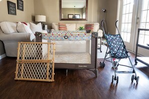 A baby playpen with a colorful play mat, a wooden gate, and a stroller in a living room with a sofa and a mirror. - Welcoming 4 BR Sleeps 10 Guests Wl2901 (Kissimmee)