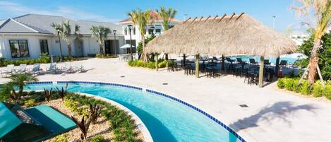 Zona de piscina con sillones de descanso, una sombrilla de paja y una piscina con borde azul.
