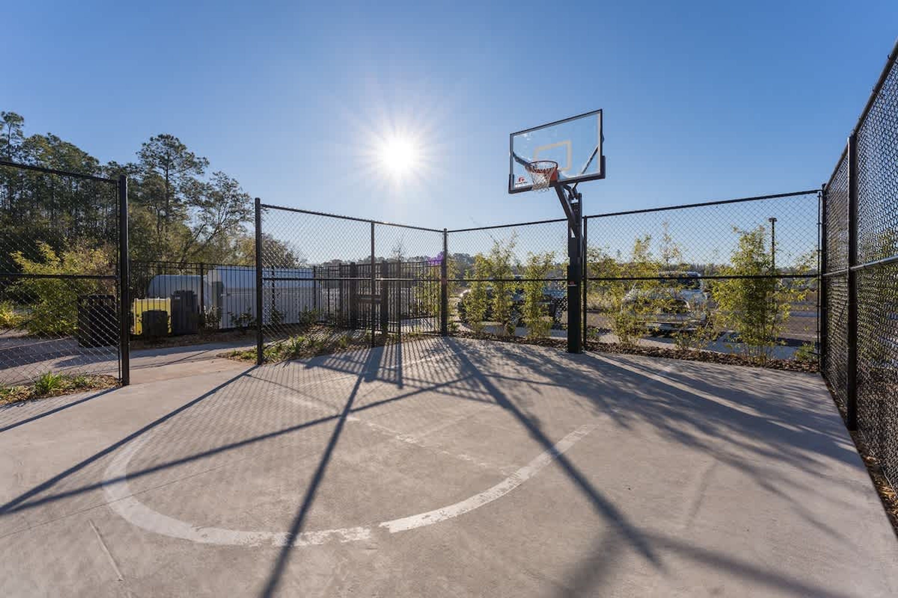 Een buitenbasketbalveld met een hek van gaas, een basketbalring en een heldere lucht.
