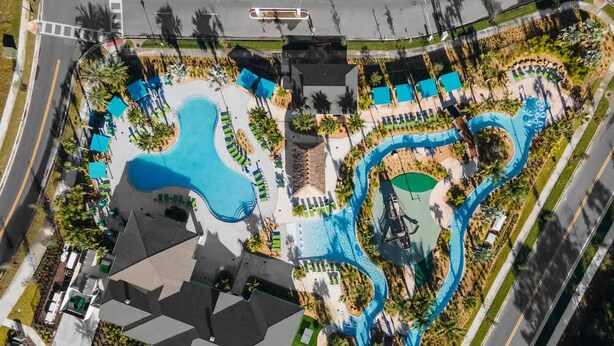 An aerial view of a resort with multiple swimming pools, a helicopter landing pad, and a parking area.