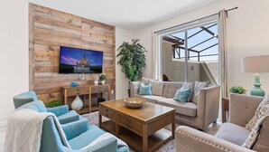 A living room with a wooden wall, a TV mounted above a wooden coffee table, a sofa, and a large window with curtains.