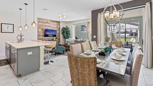 A modern kitchen with a central island, a dining area with a table set for four, and a living area with a sofa and TV.