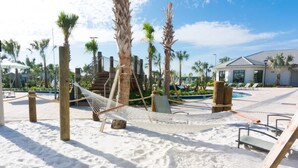 A sandy beach area with a hammock, palm trees, and a pool.