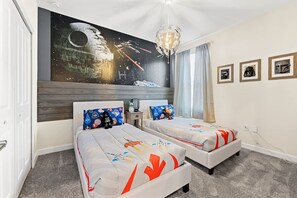 A bedroom with two beds, a mural of a space scene, and framed items on the wall.