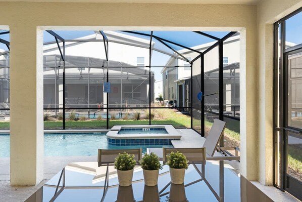 A glass-enclosed patio with a pool and hot tub, outdoor seating, and potted plants.