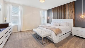 Ein Schlafzimmer mit einem Bett, einer Bank, einem Schminktisch und einer Wandleuchte.