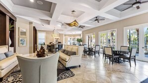 A spacious living area with a sofa, dining table, and chairs, a ceiling fan, and large windows allowing natural light.