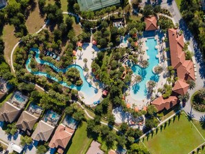 Luchtbeeld van een resort met meerdere zwembaden, weelderige begroeiing en diverse gebouwen.