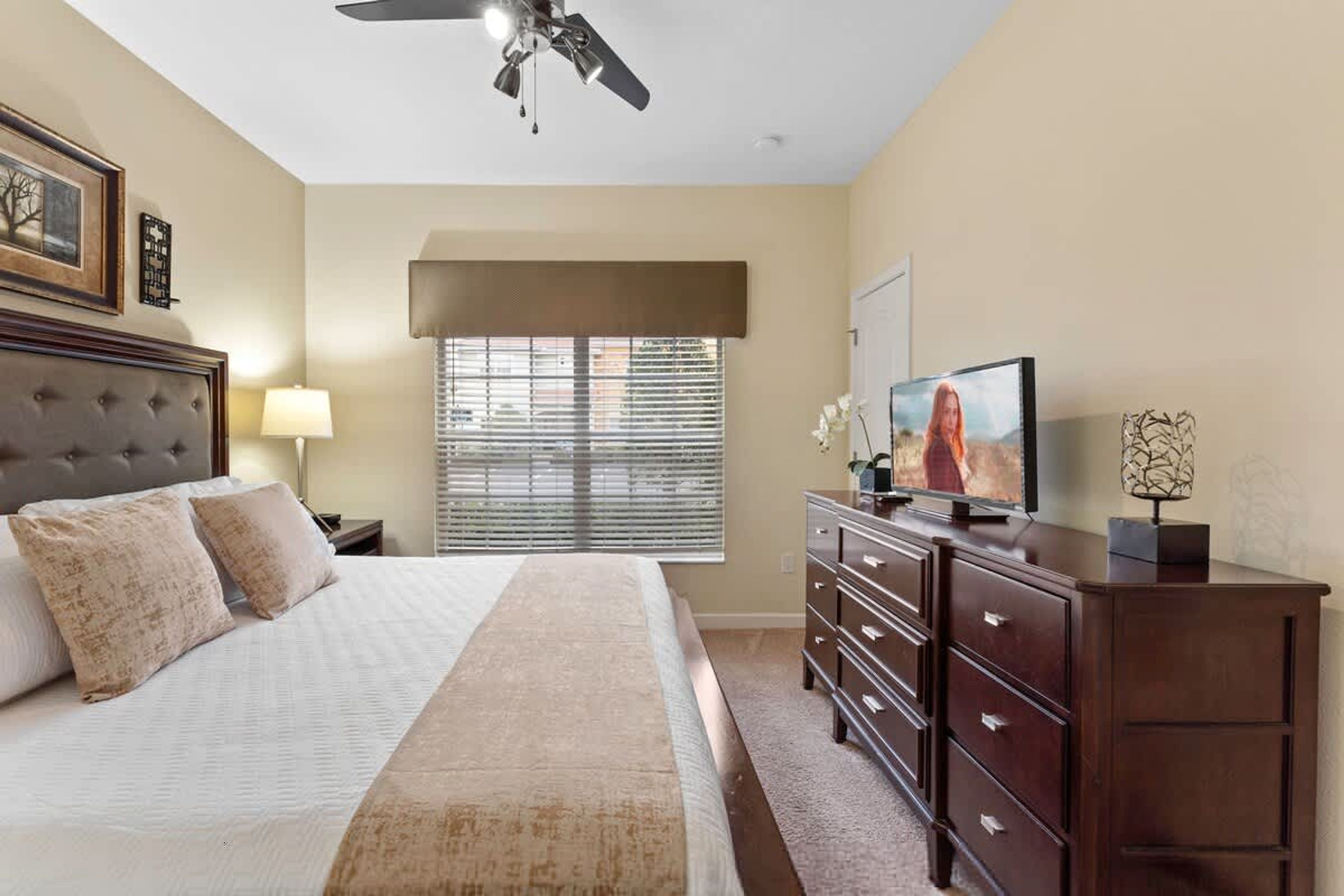 Quarto com uma cama grande, cômoda, televisão e ventilador de teto.