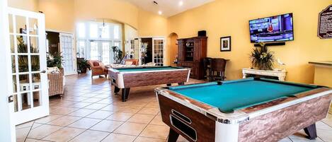 A pool area with two pool tables, a television mounted on the wall, and a door leading to another room.