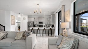 A modern kitchen with white cabinets, a central island with stools, and a dining area with a table and chairs. - Luxury Decor 6BR at Storey Lake Sleeps 16 Sl2945 (Kissimmee)
