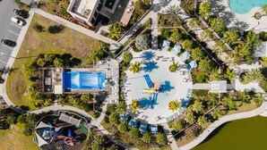 Luchtbeeld van een resort met een centraal gelegen zwembad, een apart gebouw met een blauw dak en een fontein.