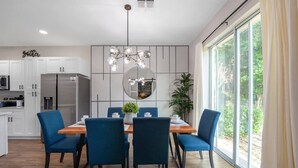 A modern kitchen with white cabinets, a stainless steel refrigerator, and a dining area with blue chairs and a wooden table. - New Listing - Modern Decor 4 BR Townhouse (Kissimmee)