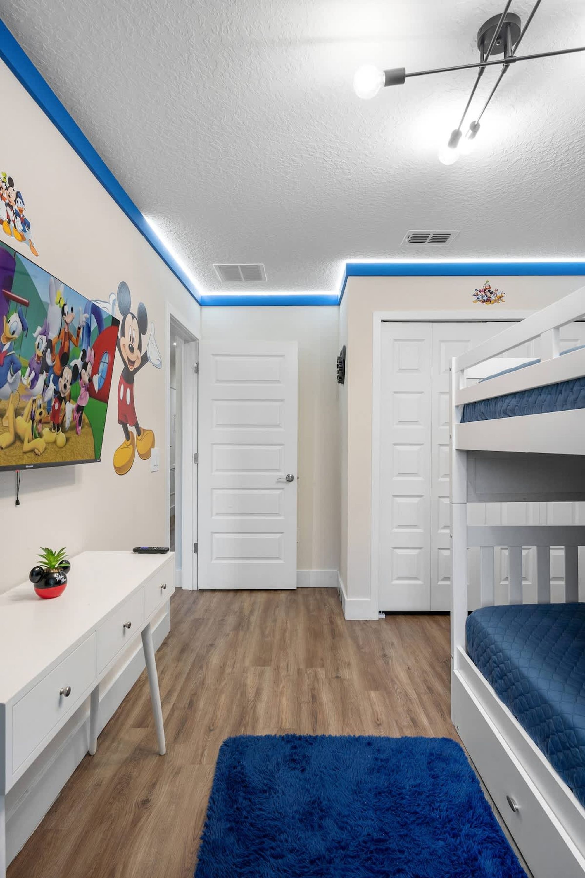 Una habitación infantil con literas, un escritorio y un gran mural de dibujos animados en la pared.