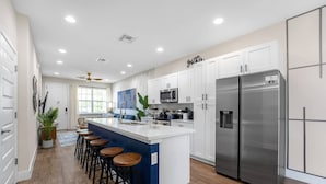 A modern kitchen with white cabinets, a stainless steel refrigerator, and a blue accent wall. - New Listing - Modern Decor 4 BR Townhouse (Kissimmee)