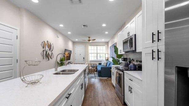 A modern kitchen with white cabinetry, a large island with a sink, and a dining area with a blue sofa. - New Listing - Modern Decor 4 BR Townhouse (Kissimmee)