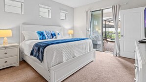A bedroom with a white bed, two bedside lamps, a nightstand, and a view of an outdoor patio through a glass door. - Pet Friendly Amazing 5 BR Sleeps 10 Ww2116 (Kissimmee)