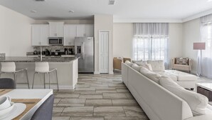 A modern kitchen with white cabinets, a central island, and a dining area with chairs.