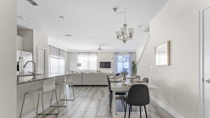 A modern kitchen with a central island, a dining area with a table and chairs, and a living space with a sofa and a TV.