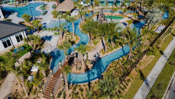 Eine Vogelperspektive zeigt einen luxuriösen Urlaubsort mit mehreren Swimmingpools, Palmen und einer gepflegten Landschaft.