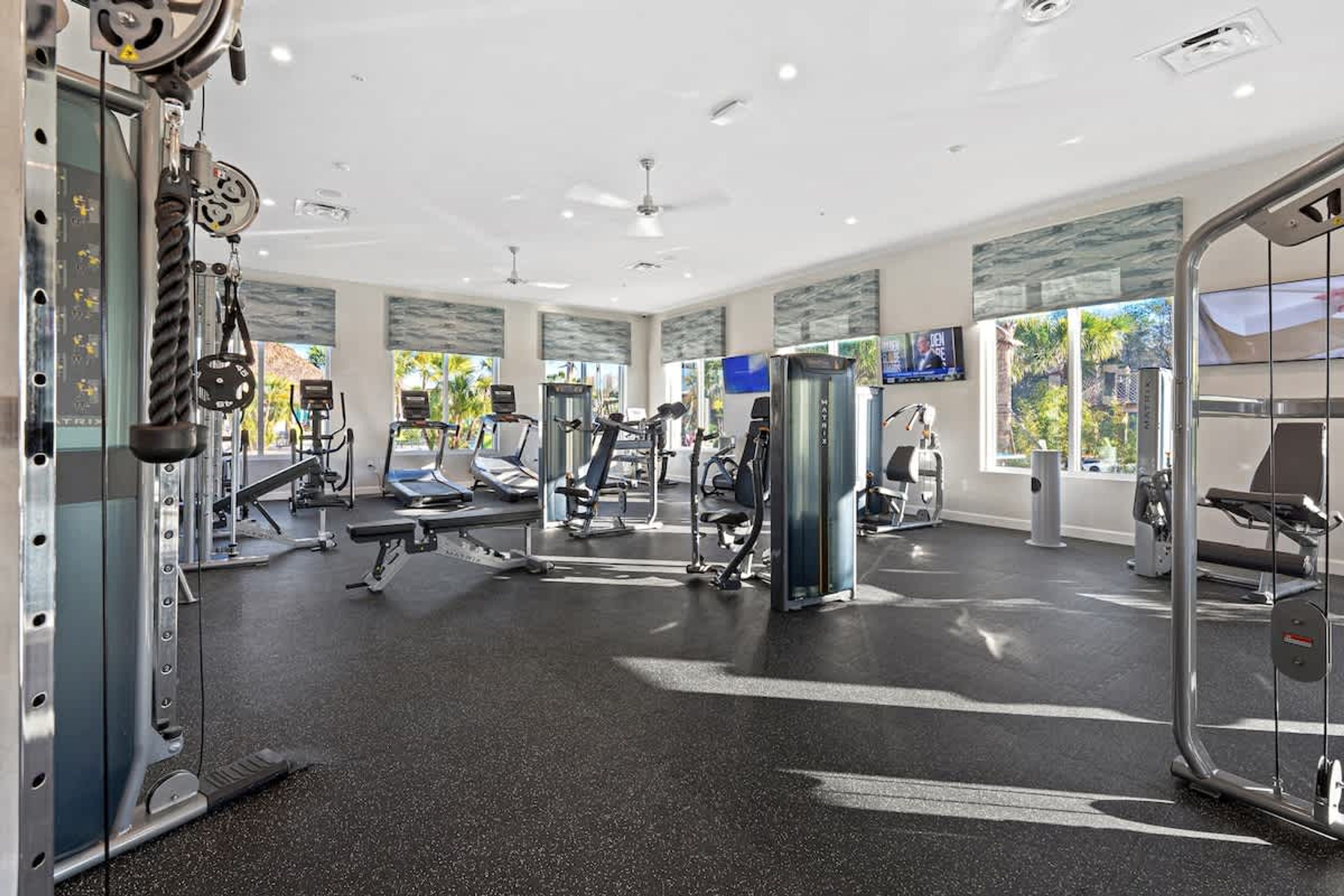 A modern gym with various exercise equipment, large windows, and a clean, spacious layout.