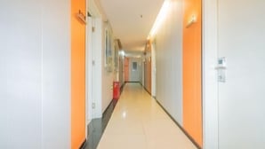 A long, narrow hotel corridor with white walls and orange accents, leading to a door at the end. - Puhua Hotel (Shanghai)