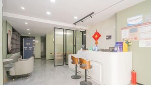 A reception area with a white counter, two bar stools, a red decorative hanging, and a fire extinguisher. - Puhua Hotel (Shanghai)