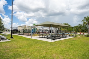 Un área de picnic techada con bancos y un parque infantil al fondo.