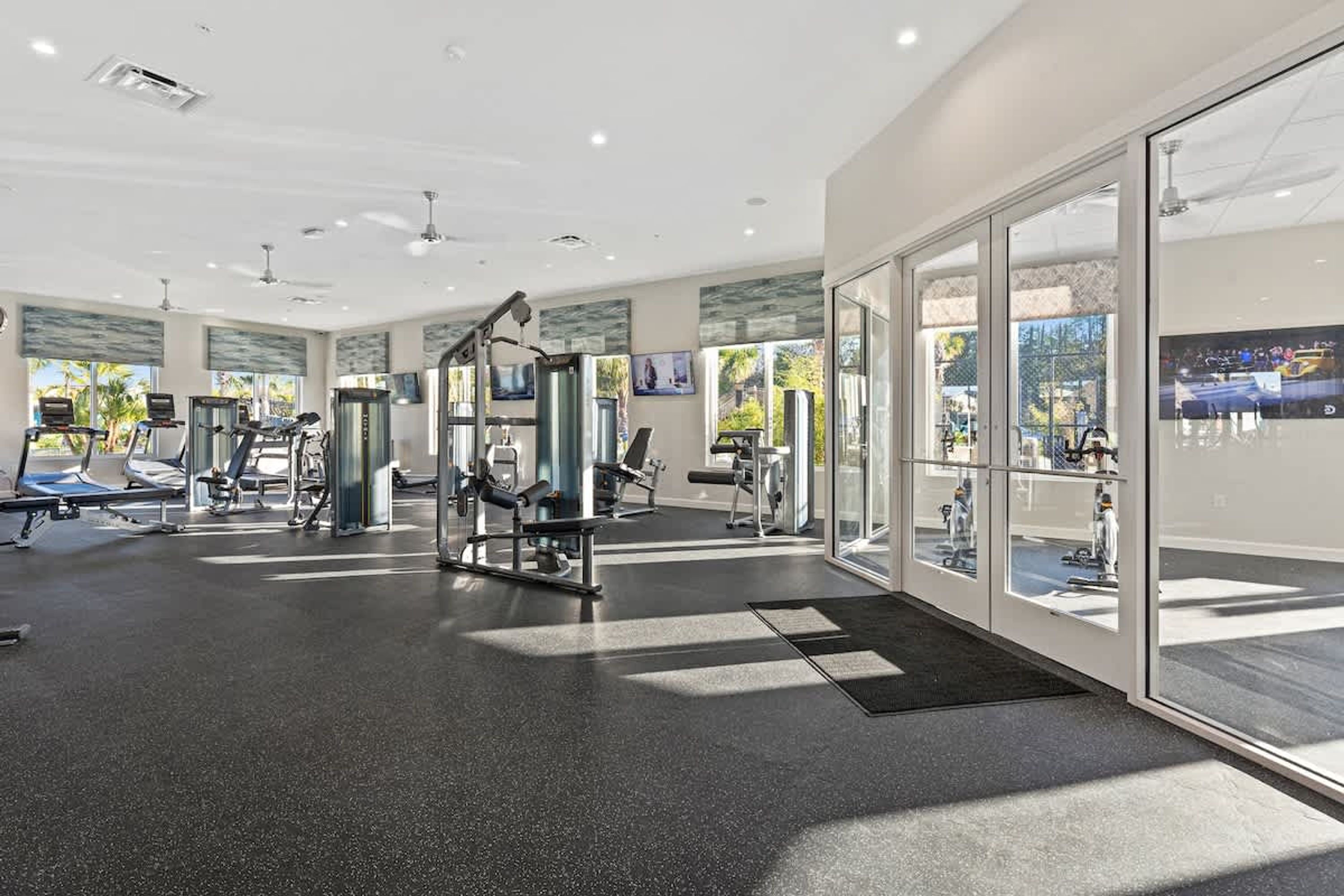 A modern gym with various exercise equipment, large windows, and a clean, well-lit interior.