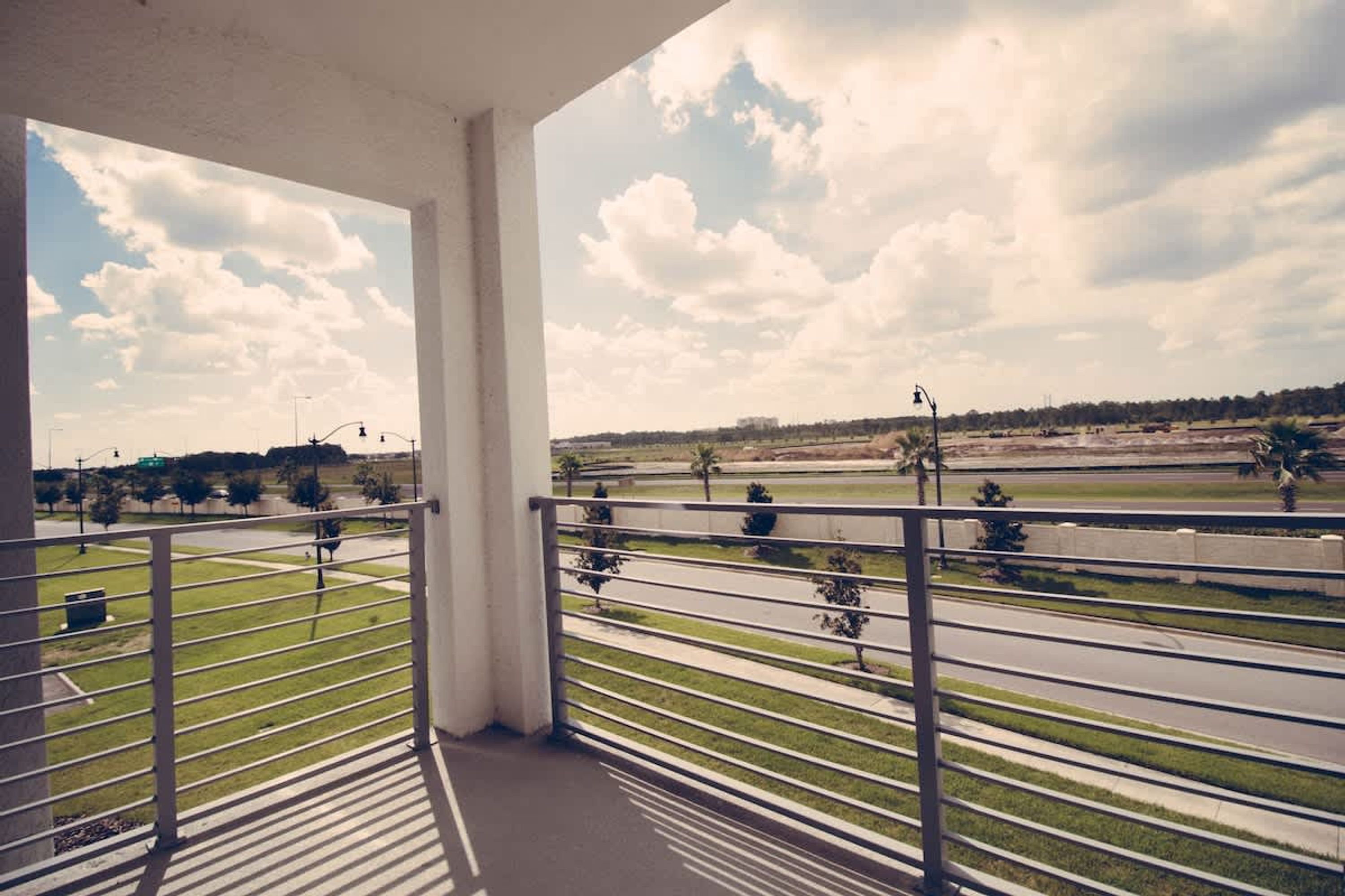 Varanda com vista para uma estrada e vegetação, com grade de metal e céu claro.