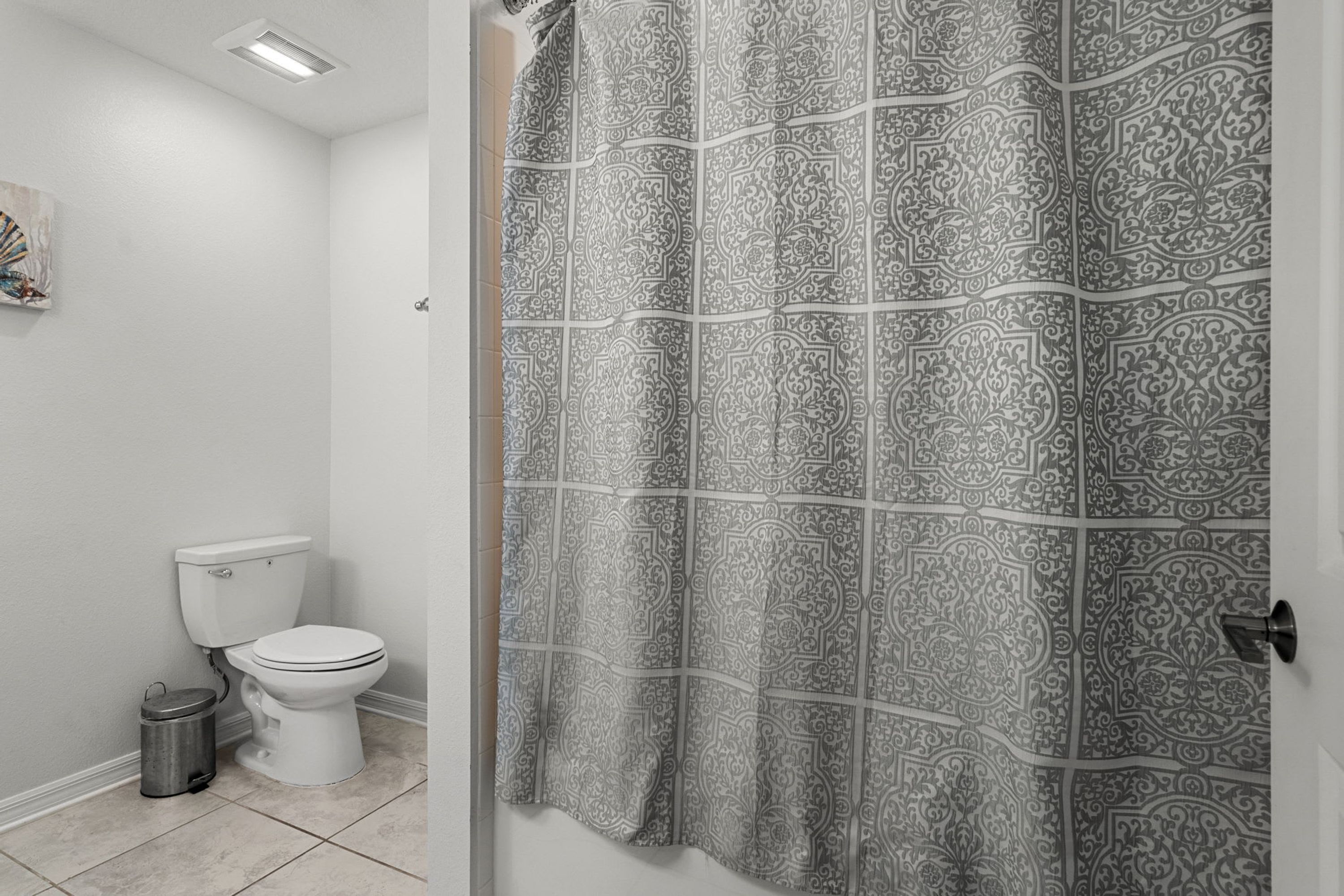 A bathroom with a toilet, a trash can, and a shower curtain with a geometric pattern.