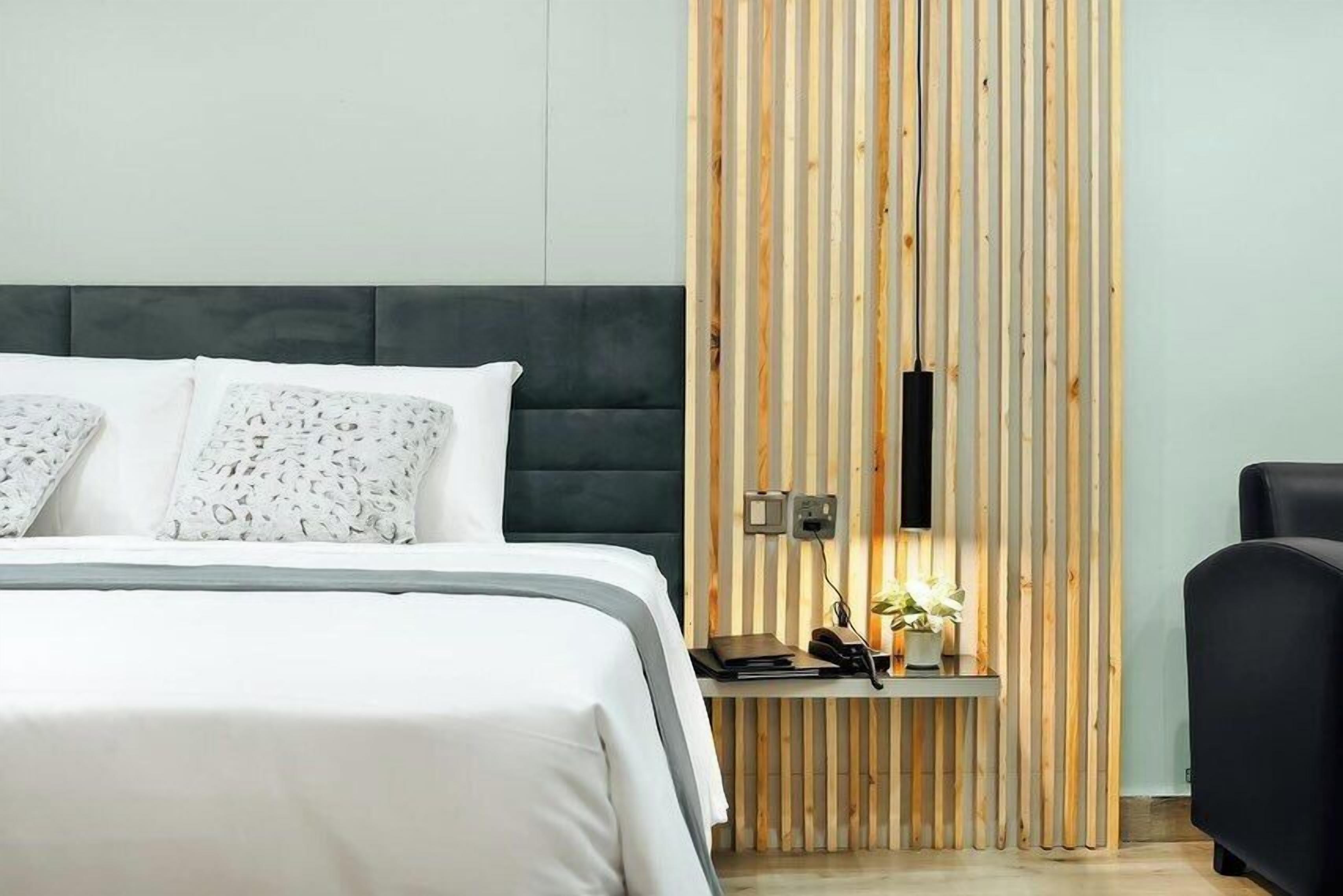 A modern hotel room with a bed, a desk with a phone and a plant, and a wooden panel wall.