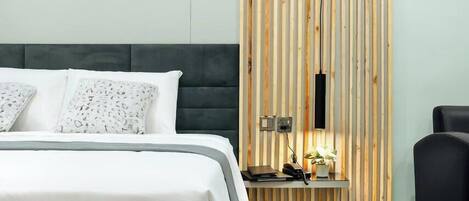 A modern hotel room with a bed, a desk with a phone and a plant, and a wooden panel wall.