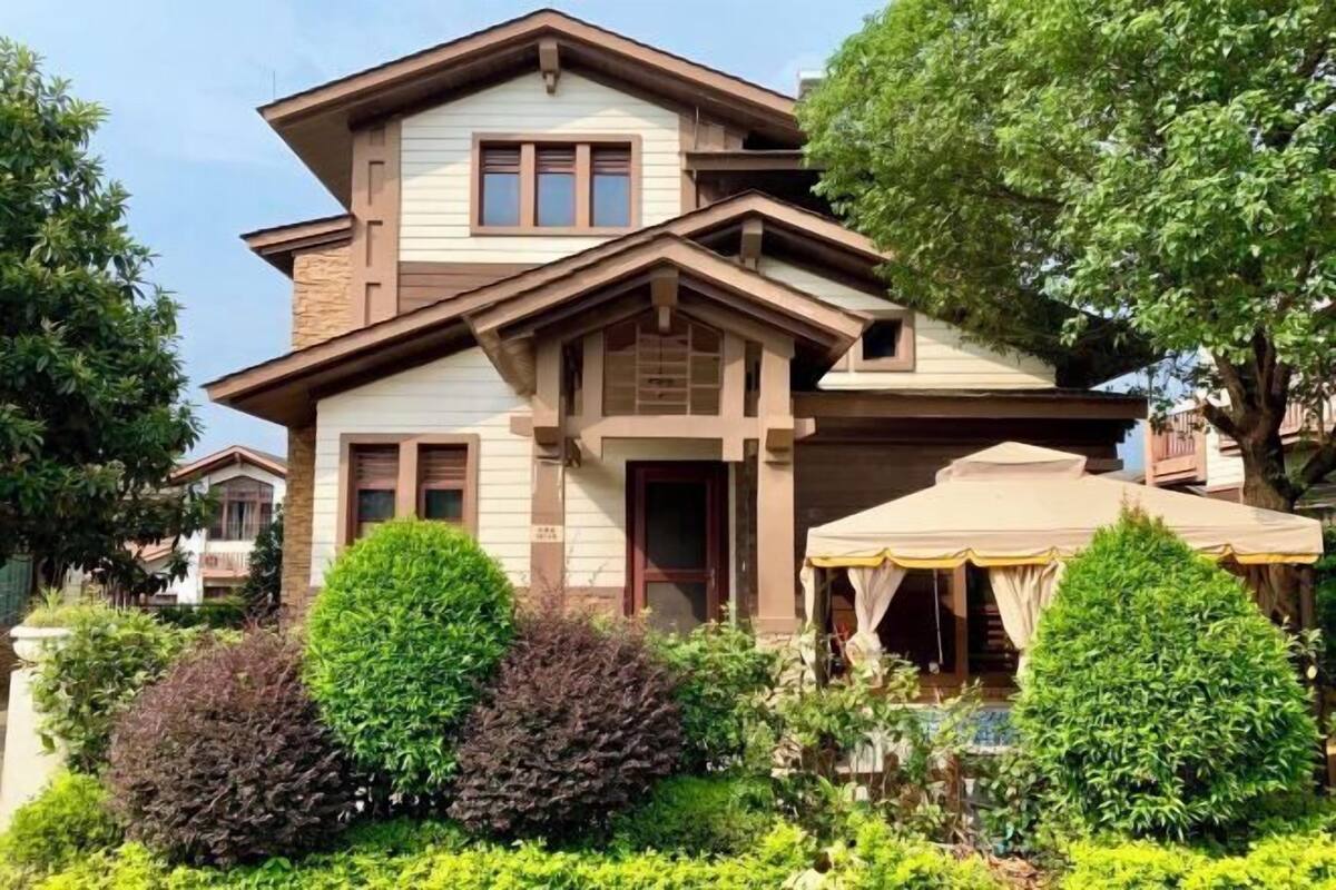 A two-story house with a balcony, a covered patio, and well-maintained hedges.