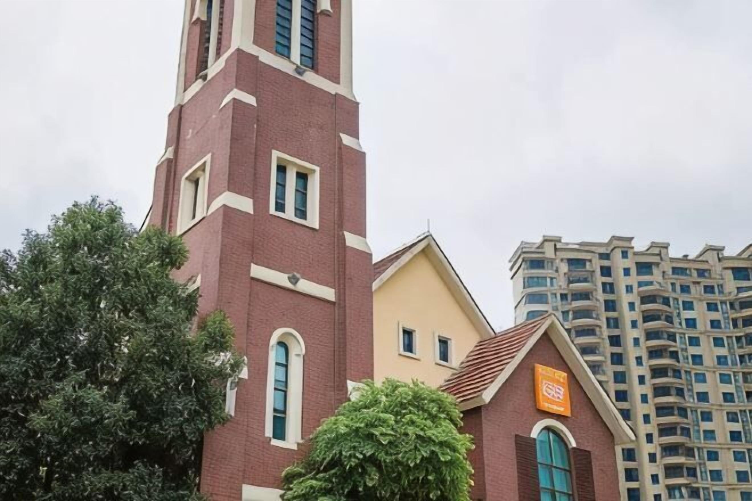 Una iglesia con un campanario alto y un edificio más pequeño con un letrero.