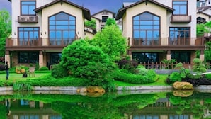 A multi-story building with balconies, a pond, and lush greenery. - Country Garden Hot Spring Holiday Villa (Fogang)
