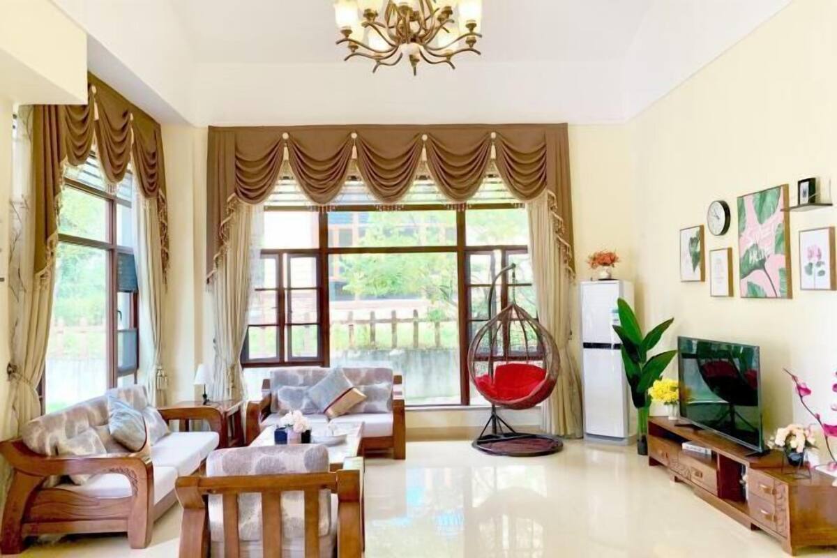 A spacious living room with a sofa, chairs, a hanging chair, a TV, and a refrigerator.