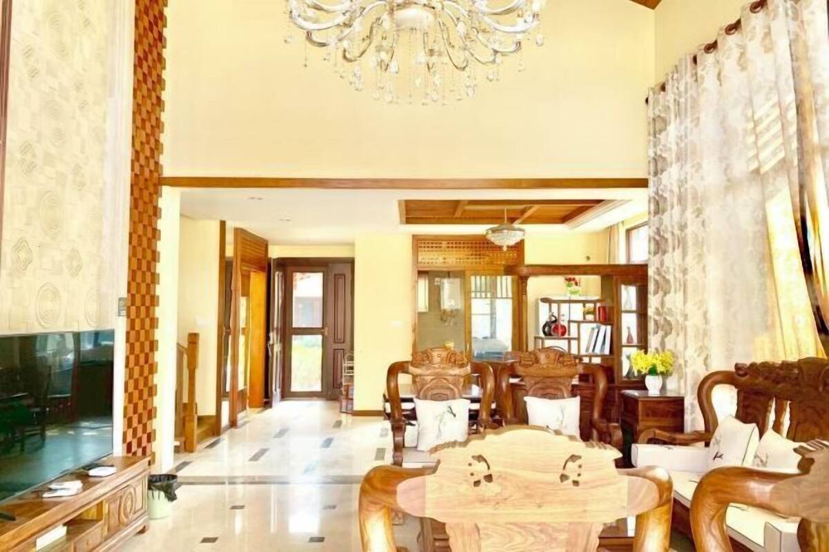 A spacious living room with a wooden dining table, comfortable seating, a chandelier, and a television.