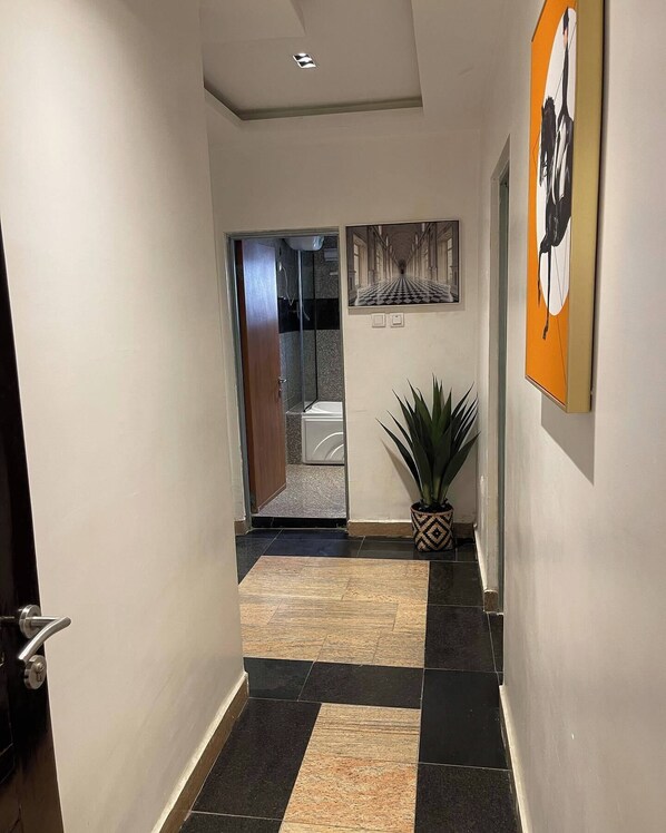 A hallway with a tiled floor, a potted plant, and a framed artwork on the wall.