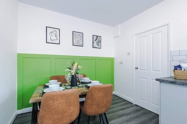 Un coin repas agrémenté d’un mur d’accent vert, d’une table dressée pour deux personnes et d’œuvres d’art encadrées au-dessus.