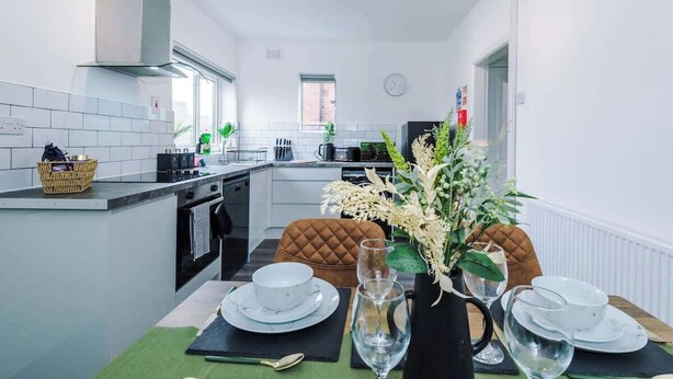 Una cucina moderna con piastrelle bianche, un'isola centrale e un'area pranzo con un tavolo apparecchiato per due.