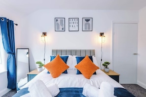 Une chambre d’hôtel avec un lit, deux tables de chevet, un miroir, une porte et trois tableaux encadrés accrochés au mur.