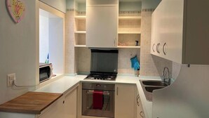 Una cocina compacta con armarios blancos, horno integrado, cocina a gas y un lavabo.