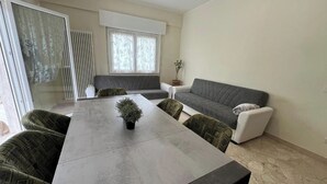 Una sala de estar moderna con un sofá gris, una mesa de comedor con cuatro sillas y una planta en maceta.