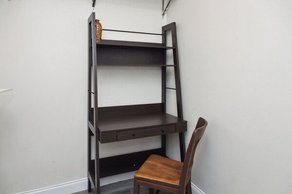 A corner room with a built-in dark wooden desk and chair, a ladder shelf, and a small decorative item on the top shelf.