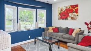 A living room with a grey sofa, a glass coffee table, and a painting of flowers on the wall. - Charming 3-bedroom house with AC, WiFi located in Supply NC near Holden Beach (supply)