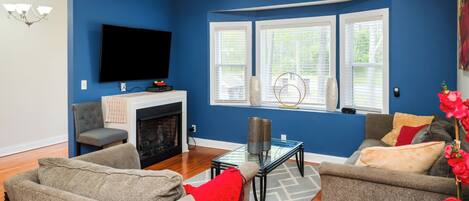 A living room with a fireplace, two sofas, a TV, and a window with blinds.