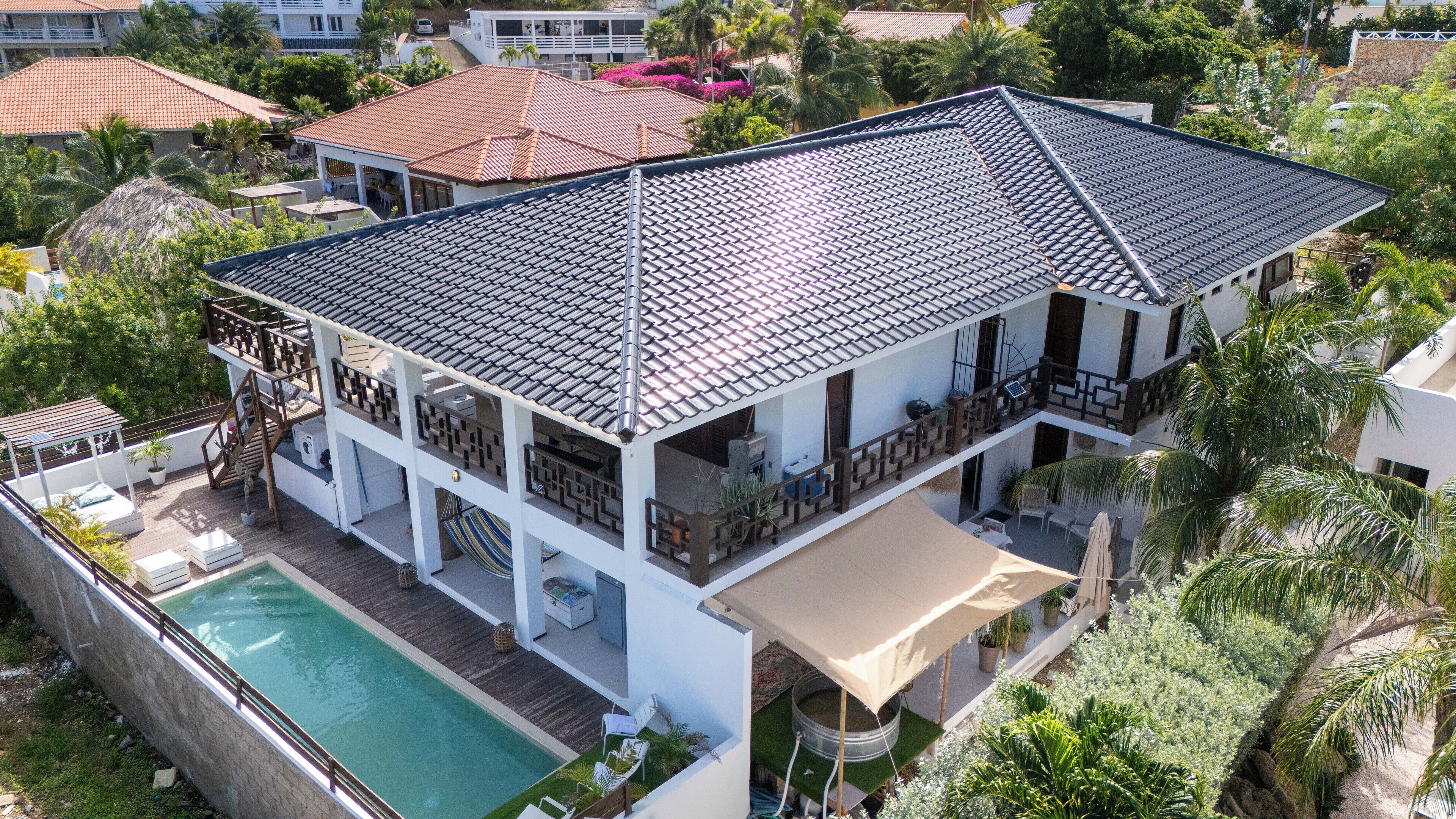 A two-story house with a tiled roof, a swimming pool, and a covered patio area.