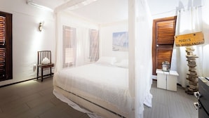 A bedroom with a four-poster bed, a wooden chair, a nightstand, and a stone pillar. - Mi Cuna Stays Collection (Jan Thiel)