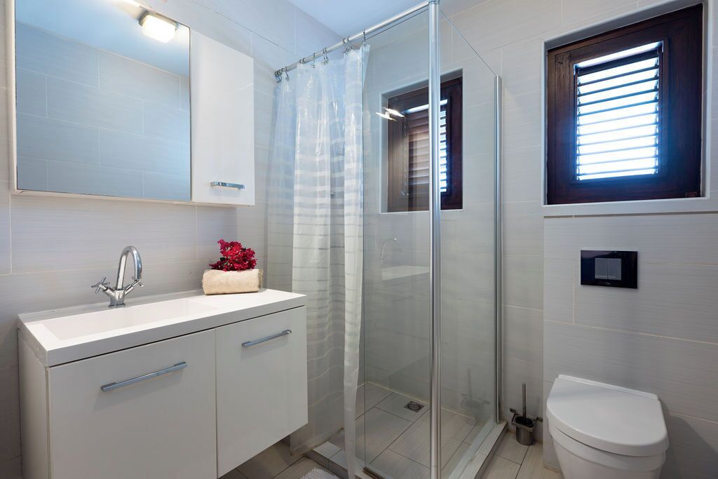 Un baño moderno con cabina de ducha de vidrio, un lavamanos blanco con espejo y un inodoro.